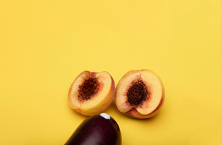 Two peach halves and an eggplant on a yellow background arranged in a sexual innuendo style.