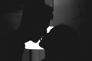 Silhouetted couple about to kiss in a dimly lit room with a soft light in the background.